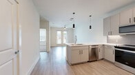 Located at 400 W. Main St in Lewisville, TX, this well-appointed one-bedroom, one-bathroom residence offers a thoughtfully designed open-concept layout. Light wood-look flooring flows throughout the main living areas, creating a bright and cohesive aesthetic. The combined living, dining, and kitchen area serves as the heart of the home, anchored by a sleek kitchen peninsula with a white quartz countertop and undermount sink. The kitchen is equipped with stainless steel appliances—including a refrigerator, range, microwave, and dishwasher—complemented by two-tone cabinetry in white and warm greige with a classic subway tile backsplash. Stylish cylindrical pendant lights add a modern finishing touch. The living area opens to a private balcony through glass French doors, with a ceiling fan overhead enhancing airflow and comfort. The bedroom features soft carpeting, a large window for natural light, and direct access to the full bathroom. The bathroom offers a glass-enclosed walk-in shower with tile surround, a vanity with quartz countertop, and direct entry into a well-organized walk-in closet with built-in shelving. An in-unit laundry area completes this efficiently designed residence.
