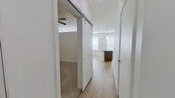 This efficiently designed one-bedroom, one-bathroom residence makes excellent use of its single-floor layout, blending modern finishes with practical living spaces throughout. The open-concept kitchen serves as a central highlight, featuring rich dark wood cabinetry extending to the ceiling, stainless steel appliances including a refrigerator, range, and over-the-range microwave, and a striking iridescent tile backsplash. A large granite-topped island with pendant lighting above anchors the space, providing both additional prep area and a natural gathering point. Light wood-tone flooring runs throughout the main living and kitchen areas, contributing to a bright and cohesive aesthetic. A sliding barn door adds a contemporary architectural detail at the hallway entrance, connecting the main living area to the private quarters. The bedroom is a comfortable, carpeted retreat equipped with a ceiling fan and clean white walls, offering a calm and restful environment. A dedicated closet provides practical storage. The bathroom is cleanly finished with wood-tone cabinetry, dark stone countertops, light wood-tone flooring, and a full tub-shower combination with large-format tile surround and a sleek sliding glass door. Natural light filters in through multiple windows fitted with blinds, enhancing the overall brightness and open feel of the space.