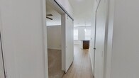 This efficiently designed one-bedroom, one-bathroom residence makes excellent use of its single-floor layout, blending modern finishes with practical living spaces throughout. The open-concept kitchen serves as a central highlight, featuring rich dark wood cabinetry extending to the ceiling, stainless steel appliances including a refrigerator, range, and over-the-range microwave, and a striking iridescent tile backsplash. A large granite-topped island with pendant lighting above anchors the space, providing both additional prep area and a natural gathering point. Light wood-tone flooring runs throughout the main living and kitchen areas, contributing to a bright and cohesive aesthetic. A sliding barn door adds a contemporary architectural detail at the hallway entrance, connecting the main living area to the private quarters. The bedroom is a comfortable, carpeted retreat equipped with a ceiling fan and clean white walls, offering a calm and restful environment. A dedicated closet provides practical storage. The bathroom is cleanly finished with wood-tone cabinetry, dark stone countertops, light wood-tone flooring, and a full tub-shower combination with large-format tile surround and a sleek sliding glass door. Natural light filters in through multiple windows fitted with blinds, enhancing the overall brightness and open feel of the space.