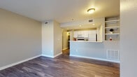This single-floor residence is thoughtfully laid out to maximize functionality and comfort. The living area is open and airy, featuring warm-toned walls, clean white baseboards, and rich wood-look plank flooring that flows throughout the main living spaces. A built-in fireplace with a tiled surround serves as a focal point in the living room, complemented by a window that brings in natural light and outdoor views of surrounding greenery.

The kitchen is well-appointed with white cabinetry, white appliances including a range, microwave, and refrigerator, as well as a stainless steel sink and light countertops. A peninsula counter with open shelving above connects the kitchen to the living area, creating a practical and social layout. Multiple closeted storage areas and a pantry door provide ample organization.

The bedroom is generously sized, finished with plush carpet, and features a sliding glass door leading to a private patio with outdoor views. A ceiling fan adds comfort, and a walk-in closet with built-in shelving provides excellent storage.

The bathroom is designed with accessibility in mind, equipped with sturdy grab bars near the shower and toilet, and finished with wood-look flooring for continuity throughout the space.