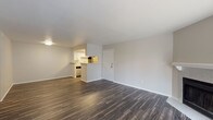 This single-floor residence offers a clean, modern aesthetic with a thoughtfully designed layout. The open living area is anchored by rich, dark hardwood-style flooring that extends throughout the main living spaces, creating a warm and cohesive feel. A standout feature of the living room is the classic fireplace with a white surround, complemented by a sliding glass door that floods the room with natural light and provides access to an outdoor area. The kitchen is positioned in an open-concept layout adjacent to the entry, featuring white cabinetry, a stainless steel electric range with overhead ventilation, and a pass-through counter that keeps the space connected and functional. The bedrooms are carpeted in neutral tones, offering a comfortable retreat. One bedroom benefits from two windows that invite generous natural light, while another includes a sliding closet door. A walk-in closet with built-in shelving provides excellent storage. The bathrooms are finished with white tile tub-shower combinations and brushed nickel fixtures. One bathroom features a granite-topped vanity with white cabinetry and wood-look tile flooring, adding a refined touch. Throughout, the space maintains a neutral, light-filled palette that enhances its open and inviting atmosphere.