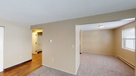 Located at 8388 Pardee Rd in Cicero, NY, this single-floor unit offers a practical and straightforward layout designed for comfortable everyday living. The floor plan, visible in the 3D overview, reveals a well-organized arrangement of interconnected living spaces with a clear separation between the kitchen and living areas.

The main living area is generously proportioned, featuring neutral-toned carpet and large sliding glass doors that allow natural light to fill the space while providing outdoor access. Baseboard heating runs along the perimeter, ensuring efficient warmth throughout. An additional window further supplements natural light on one side of the room.

The kitchen is equipped with warm, medium-toned wood cabinetry extending to the upper and lower walls, light-colored countertops, and a white electric range. The hardwood-style flooring in the kitchen adds a distinct contrast to the carpeted living spaces, and a louvered storage closet provides convenient pantry space nearby.

The bedrooms are carpeted and well-sized, each featuring closets and windows that bring in natural light. Baseboard heaters are present in each room. The full bathroom includes a soaking tub with shower, a wood-framed vanity with mirror, a toilet, and durable hardwood-style flooring, creating a clean and functional space. Neutral wall tones carry consistently throughout the unit.
