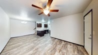 This two-story space offers a thoughtfully designed open-concept main level that seamlessly connects the living and kitchen areas. The living space is finished with warm, wood-look luxury vinyl plank flooring that extends throughout, creating a cohesive and easy-to-maintain surface underfoot. A ceiling fan with an integrated light fixture anchors the living area, complementing a decorative chandelier visible in the adjoining dining space.

The kitchen features dark espresso-toned cabinetry paired with light-toned countertops, providing a striking contrast. A peninsula-style counter extends into the open area, offering additional workspace and a casual seating opportunity. Stainless steel appliances are integrated into the kitchen layout. Neutral white walls throughout the main level create a bright, clean backdrop that enhances the sense of openness.

A staircase visible from the main level leads to the second floor, adding a multi-dimensional layout to the home. Recessed lighting in the kitchen supplements natural and ambient light across the space. The overall design aesthetic is modern and functional, with clean lines and a neutral palette that offers versatility for a variety of interior styles.