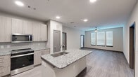 Located at 17448 N Eldridge Parkway in Tomball, Texas, this well-appointed 2-bedroom, 1-bathroom residence offers a thoughtfully designed single-floor layout with contemporary finishes throughout. The open-concept living and kitchen area serves as the heart of the home, where wood-look plank flooring, recessed lighting, and a ceiling fan create a comfortable, modern atmosphere. Multiple windows fitted with horizontal blinds allow natural light to fill the space. The kitchen is a standout, featuring a granite-topped island with a built-in sink, light wood cabinetry extending to the ceiling, a subway tile backsplash, and a full suite of stainless steel appliances including a refrigerator, range, and over-the-range microwave. The living area is generously sized with a ceiling fan and multiple windows. Both bedrooms are well-proportioned; the primary bedroom offers plush carpeting, a ceiling fan, and ample natural light, while the second bedroom features wood-look flooring and a large window. The bathroom includes a dual-sink granite vanity with modern cabinetry and a large mirror. A dedicated laundry room houses a full-size washer and dryer with overhead shelving for added storage convenience.