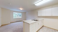 This single-floor unit is designed with a practical, open-concept layout that connects the kitchen and living area seamlessly. The kitchen is equipped with white cabinetry providing ample upper and lower storage, light-toned countertops, a double-basin sink set into a peninsula, a coil electric range, and a full-size refrigerator. The peninsula separates the kitchen from the carpeted living area, creating a natural division while maintaining an open feel. Tile flooring runs through the kitchen and connecting hallway, while soft carpet covers the living and bedroom spaces.

The living area benefits from a large window that invites natural light and offers views of the surrounding neighborhood. A baseboard heating system runs along the exterior wall, providing efficient climate control. The bedroom is generously sized, also featuring a window and baseboard heater, with a dedicated closet for storage.

A hallway connects the main living spaces to the bathroom, which includes a toilet, vanity with sink, and a shower-tub combination. A closet in the hallway offers additional storage. Throughout the unit, neutral cream and beige tones create a clean, understated aesthetic that is easy to personalize.