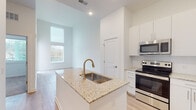 Located at 680 Hamilton Ave SE in Atlanta's Grant Park area, this single-floor residence offers a clean, contemporary design throughout. The open-concept kitchen is a standout feature, anchored by a central island with granite countertops, an undermount sink, and a brushed gold faucet. White shaker-style cabinetry lines the walls, complemented by stainless steel appliances including a French door refrigerator, electric range, over-the-range microwave, and dishwasher — providing a fully equipped cooking environment. Light hardwood-style flooring flows through the main living areas, enhancing the bright, airy atmosphere created by recessed lighting and tall windows that invite natural light. The living area is generously proportioned with clean white walls and access to an outdoor space. Bedrooms offer a calm retreat; one features soaring ceilings with tall windows framing neighborhood views, while another is finished with plush carpeting and a wide window overlooking the surrounding area. The bathroom is appointed with granite vanity countertops, white cabinetry, a large mirror, and a tiled shower-tub combination, maintaining the cohesive modern aesthetic found throughout the unit.