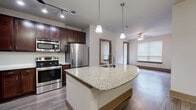Located at 155 Birdsall St in Houston's 77007 zip code, this single-story residence offers a well-designed layout with contemporary finishes throughout. The kitchen serves as the heart of the home, featuring rich dark-wood cabinetry, a subway tile backsplash, and a full suite of stainless steel appliances including a refrigerator, range, and built-in microwave. A curved granite-topped island with an integrated sink and pendant lighting overhead provides both prep space and casual seating, flowing naturally into the open living area. Wood-look hard flooring extends throughout the main living spaces, complemented by a ceiling fan and multiple windows fitted with blinds that allow for natural light control. The bedrooms are carpeted for comfort, each offering windows that bring in natural light. The primary bedroom suite includes access to a walk-in closet with wire shelving and a private en-suite bathroom. The bathrooms are finished with large-format tile flooring, dark wood vanities, granite countertops, and framed mirrors. A second bathroom mirrors the same refined aesthetic. The home's neutral color palette, two-panel interior doors in a warm taupe finish, and consistent use of quality materials create a cohesive and polished living environment throughout.