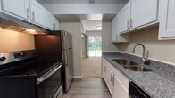 The Gallup's two-bedroom, one-bathroom unit is a single-story residence designed with a practical and comfortable layout. The kitchen serves as a functional centerpiece, featuring granite countertops, white shaker-style cabinetry with brushed nickel hardware, and a full suite of stainless steel appliances, including an electric range with overhead ventilation hood and a refrigerator. Wood-look flooring runs throughout the kitchen, providing a clean, low-maintenance surface.

The generously sized living area is carpeted and bathed in natural light, thanks to sliding glass doors that open to an outdoor view of greenery, creating a bright and open atmosphere. A structural beam detail adds a subtle architectural element to the ceiling.

Both bedrooms are carpeted and well-lit, with large windows that bring in natural light and outdoor views. One bedroom features a tall window, while the other also benefits from a sliding glass panel. Ample built-in closet storage with bifold doors and shelving is a notable feature of the bedrooms.

The bathroom is finished with granite countertops, a white vanity with a framed mirror, wood-look flooring, and a full tub-shower combination with tile surround, providing a clean and cohesive aesthetic throughout.