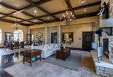 Located at 9150 S Coulter St in Amarillo, Texas, this single-floor space delivers an impressive blend of rustic elegance and refined design. The interior is defined by soaring coffered ceilings with dark wood beam detailing, which lend a grand, structural character to the open layout. Stately stone columns frame the main gathering areas, creating natural transitions between zones while reinforcing the space's warm, Tuscan-inspired aesthetic.

Flooring throughout alternates between richly stained dark hardwood and large-format travertine tile, grounding the space in earthy, durable materials. Oversized arched windows along multiple walls usher in generous natural light, brightening the warm golden tones of the textured walls. A set of French doors provides a welcoming entry with views to the outdoors.

A formal dining area accommodates a large table beneath an ornate wrought-iron chandelier, while the main living area features a stone fireplace and a comfortable seating arrangement. A pass-through service window with granite countertop hints at catering or hospitality functionality. Recessed lighting and additional chandeliers ensure a well-lit atmosphere at any hour. The overall ambiance is warm, spacious, and versatile — well-suited for gatherings, events, or community use.
