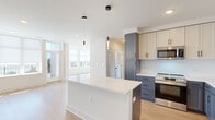 This thoughtfully designed 2-bedroom, 2-bathroom residence at 2105 Bond St in Charlottesville, Virginia offers a clean, modern aesthetic across a single-level, open-concept floor plan. Light hardwood flooring flows seamlessly throughout the main living areas, enhancing the bright and airy atmosphere created by expansive windows that invite generous natural light.

The kitchen serves as the heart of the home, featuring a large central island with a white quartz countertop, two-tone cabinetry in slate grey and cream, a white subway tile backsplash, and a full suite of stainless steel appliances including a refrigerator, range, and built-in microwave. Sleek pendant lighting above the island adds a stylish accent. The kitchen opens directly into the living area, which is lined with large windows offering outdoor views of the surrounding neighborhood.

The primary bedroom is a well-proportioned retreat, bathed in natural light through a bank of windows with serene tree-line views. The second bedroom is equally bright with its own window and light wood flooring. Both rooms provide a calm, neutral palette.

The primary bathroom features large-format tile flooring, a glass-enclosed walk-in shower with full tile surround, a single vanity with marble-look countertop, and dark cabinetry hardware. The second bathroom offers a tiled tub-shower combination with matching flooring and a compact vanity, maintaining the same refined aesthetic throughout.