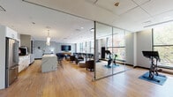 Located at 66 Summer St in downtown Stamford, Connecticut, this thoughtfully designed amenity floor seamlessly combines fitness, work, and relaxation into a single, cohesive space. Wide-plank hardwood flooring flows throughout, unifying the various zones beneath a clean, contemporary ceiling with recessed lighting.

The fitness area is divided into two distinct sections. A dedicated cardio room lines an entire wall of floor-to-ceiling windows, flooding the space with natural light and offering views of the surrounding streetscape. It is equipped with treadmills, ellipticals, and stationary bikes. Adjacent to it, a separate cycling studio enclosed by sleek glass sliding partitions houses Peloton-style spin bikes, providing an on-demand boutique fitness experience.

The social and lounge area features a comfortable seating arrangement with tufted leather sofas, club chairs, and a wall-mounted flat-screen TV, creating an inviting space to unwind. A fully equipped kitchenette with white cabinetry, stainless steel appliances, and a striking marble-topped counter supports both casual gatherings and everyday convenience.

A co-working zone near the windows offers long communal tables with modern seating, bathed in natural light and framed by urban views of downtown Stamford — ideal for focused work or collaborative sessions. The overall ambiance is polished, functional, and modern.