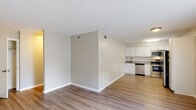 Located at 3314 Wickslow Dr in Wilmington, NC, this single-floor residence offers a clean, modern aesthetic throughout. The open-concept living and dining area is finished with light wood-look flooring and neutral gray-toned walls, creating a bright and airy atmosphere. A partial wall divides the living space from the kitchen, which features white shaker-style cabinetry, granite countertops, a classic white subway tile backsplash, and a full suite of stainless steel appliances including a refrigerator, electric range, over-the-range microwave, and dishwasher. Natural light filters in through multiple windows in the kitchen area. A closet with built-in rod and shelving is visible off the main living area, providing convenient storage. The bedroom is well-proportioned, bathed in natural light from a large window overlooking greenery, and continues the consistent wood-look flooring. A sliding glass door in one room opens directly to an outdoor deck, seamlessly connecting interior and exterior living. The bathroom includes a white vanity with an oversized mirror, decorative lighting, and a separate tiled tub-shower combination with a showerhead.