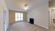This single-floor, 1-bedroom, 1-bathroom unit at Carter offers a well-organized and comfortable living space designed for practical, everyday living. The living room serves as the heart of the home, featuring soft wall-to-wall carpeting that adds warmth underfoot. A classic fireplace with a sleek black surround anchors one wall, providing a welcoming focal point ideal for relaxing evenings. A ceiling fan with integrated lighting is centrally positioned overhead, helping to maintain comfortable airflow throughout the space. The room is finished with a textured ceiling and warm neutral-toned walls that lend a clean, inviting ambiance. A large window allows natural light to fill the room, offering views to the outdoors and creating a bright, open atmosphere. White baseboards throughout provide a crisp contrast to the warm wall tones, contributing to the tidy, well-maintained appearance of the space. The overall layout of this unit reflects a straightforward, functional design that makes efficient use of the available space, making it a practical choice for individuals or couples seeking a comfortable and manageable living environment.