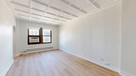 Located on the 14th floor at 1211 North La Salle Drive in Chicago's vibrant Near North Side neighborhood, this one-bedroom, one-bathroom unit offers a well-designed layout with thoughtful architectural details throughout. Light hardwood flooring flows seamlessly across the entire unit, complementing the crisp white walls and creating a bright, cohesive aesthetic.

The defining architectural feature of this unit is its striking coffered ceiling, visible in the bedroom and living areas, adding visual depth and a classic character to the space. An elegant arched doorway connects the living and sleeping areas, lending a charming, timeless quality to the interior.

The combined dining and living area provides a flexible, open space anchored by natural light from the building's windows. The galley-style kitchen is efficiently designed and features stainless steel appliances, including a refrigerator, range, and over-the-range microwave, paired with white cabinetry and a light stone countertop with a marble-effect backsplash.

The spacious bedroom accommodates the unit's largest footprint and includes two closets for generous storage. The bathroom is finished with marble-look tile flooring, a tiled tub-shower surround, a warm wood vanity with brass fixtures, and classic white fixtures throughout. The unit also includes a dedicated laundry area with shelving.
