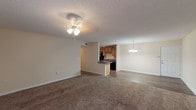 This single-story residence at Austin Park Apartments offers a thoughtfully arranged floor plan that connects the main living areas in an open, flowing layout. The expansive living room is finished with plush carpet and features a ceiling fan with light fixture overhead, alongside a textured ceiling that carries throughout the common areas. A sliding glass door fills the space with natural light and provides outdoor access. The living area transitions seamlessly into a dedicated dining space, distinguished by hardwood-style flooring and an elegant chandelier overhead.

The galley-style kitchen is well-appointed with warm wood cabinetry extending from floor to ceiling on both sides, dark laminate countertops, and a full suite of black appliances including a refrigerator, electric range, microwave, and dishwasher. Track lighting and hardwood-style flooring complete the kitchen's functional design.

The bedrooms are generously sized, each with soft carpet, ceiling-mounted light fixtures, and windows with blinds that allow for natural light. One bedroom features a tray ceiling detail, adding architectural interest. The bathrooms are clean and functional, each offering a full tub-shower combination — one with a surround enclosure and one with a standard curtain rod setup — complemented by tile flooring.