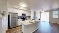 This two-story residence is designed with a clean, contemporary aesthetic and a practical open-concept layout. The kitchen serves as a central hub, outfitted with white shaker-style cabinetry, a gray subway tile backsplash, stainless steel appliances, and a peninsula with light quartz countertops that doubles as a casual dining space with a built-in sink. Wood-look flooring flows seamlessly from the kitchen into the adjoining living area, which features crown molding, a ceiling fan, a fireplace with a white mantel, and access to natural light through a large sliding glass door with vertical blinds.

The bathrooms are finished in a consistent white palette, featuring quartz-topped vanities, white cabinetry with overhead storage, and wood-look flooring. One bathroom includes a glass-enclosed shower, while another offers a full soaking tub with a shower and curtain rod. Both are compact yet efficiently arranged.

The bedrooms are carpeted for comfort and each receives natural light through sizable windows with blinds offering views of surrounding rooftops and landscaping. Ceiling fans are present in the bedrooms, contributing to a comfortable and well-ventilated atmosphere. The overall design is neutral and cohesive throughout.