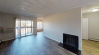 This single-floor residence offers a thoughtfully laid-out living space with a clean, neutral color palette and a mix of flooring materials that define each area. The main living room is a standout, featuring a classic wood-burning fireplace with a dark tile surround and direct access to a private balcony through a sliding glass door, allowing natural light to pour in and offering views of the surrounding landscape. Baseboard heating runs along the walls throughout the living and bedroom areas, ensuring consistent warmth.

The galley-style kitchen is efficiently designed with white cabinetry, light stone-look countertops, a stainless steel double sink, and stainless steel appliances, including a refrigerator. The wood-look luxury vinyl plank flooring extends seamlessly from the living areas into the kitchen.

The bedrooms are carpeted for comfort and feature neutral walls, textured ceilings, and generous closet space, including a built-in shelving unit and a standard reach-in closet. Natural light filters through window blinds, brightening each room.

The bathroom is well-appointed with a white tiled tub-surround combo fitted with chrome fixtures and a shower rod, alongside a separate vanity area featuring a speckled countertop, an undermount sink, and a large mirror with overhead lighting.
