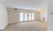 This single-floor unit is laid out with a practical, open flow connecting its key living spaces. The living room serves as the centerpiece, offering a generously proportioned area covered in neutral-toned carpet and anchored by a set of full-length French doors that span much of the exterior wall. These doors allow abundant natural light to fill the room and provide direct outdoor access. A ceiling fan is positioned overhead, and the warm, neutral wall tones contribute to a bright, airy atmosphere throughout.

Adjacent to the living area, the galley-style kitchen is efficiently organized with warm wood-toned cabinetry lining both upper and lower sections of the walls. Laminate countertops provide ample workspace, and the kitchen includes a gas range, a refrigerator, and a single-basin sink. Tile flooring runs underfoot, offering a practical contrast to the carpeted living spaces. An electrical panel is also accessible within the kitchen area.

The bedroom is a quiet, carpeted room with closet access and a window that brings in natural light. A second carpeted room visible in the floor plan provides additional flexible space. The bathroom features a full tub-shower combination, a white vanity with under-sink storage, a wall-mounted mirror cabinet, and tile flooring, all finished in a clean, all-white scheme.