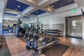 Located in Brookhaven, Georgia, this single-floor fitness center offers a comprehensive and thoughtfully designed workout facility. The space features an open, expansive layout with hardwood-style flooring, rubber exercise mats, and soaring ceilings accented by elegant coffered details with blue insets, lending the space a refined yet energizing atmosphere.

The strength training area is well-stocked with a full rack of dumbbells, kettlebells, medicine balls, resistance machines, squat racks, and benches, supported by floor-to-ceiling mirrors that visually expand the space and aid in form correction. Adjacent to this zone, a functional training area includes a punching bag, stability balls, and a BOSU trainer.

The cardio section is equipped with Matrix treadmills, indoor cycling bikes, and WaterRower rowing machines, positioned alongside large windows that frame lush outdoor greenery, providing an inspiring view during workouts. Mounted flat-screen televisions are conveniently placed throughout.

A dedicated water station with a bottle-fill fountain, sanitation dispenser, and stainless steel waste receptacles ensures cleanliness and convenience. Wainscoting and panel molding throughout reinforce a polished, upscale aesthetic. The facility also includes restroom access and ample natural light through generous window installations on multiple walls.