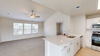 Located at 8800 N Ames Dr in Kansas City, MO, this two-story residence offers 2 bedrooms and 3 bathrooms across a well-designed floor plan. The entry level houses an attached two-car garage with an automatic opener, providing convenient access to the main living area above. The upper floor features an open-concept kitchen equipped with white shaker cabinetry, subway tile backsplash, stainless steel appliances including a French door refrigerator, and a large island with a double undermount sink and bright white countertops. A sliding glass door off the kitchen leads to an outdoor balcony. The bedrooms are carpeted and feature vaulted ceilings with ceiling fans, allowing for excellent air circulation and an airy feel. The generously sized primary bedroom includes a walk-in closet outfitted with extensive wire shelving and hanging systems. Each of the three bathrooms is finished with light wood-look tile flooring, white vanity cabinetry, and a tub-shower combination. The overall aesthetic throughout is clean and contemporary, with a neutral palette of whites and soft beiges that create a bright, cohesive atmosphere across every room.