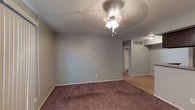 This single-floor residence offers a functional and straightforward layout across several well-defined living spaces. The living room is a comfortable, open area finished with plush carpeting, a ceiling fan with light fixture, and a sliding glass door dressed with vertical blinds that allows natural light to filter in. A pass-through opening connects the living area to the kitchen, adding an open feel between the two spaces. The galley-style kitchen is efficiently designed with dark wood cabinetry lining both sides, granite-style countertops, hardwood-style flooring, and black appliances including a refrigerator and electric range with overhead exhaust. A door at the end of the kitchen leads to additional storage or utility space. The bedrooms are carpeted and each feature ceiling fan and light combinations. One bedroom includes a walk-in closet with multiple shelving tiers and a built-in rod, as well as direct access to a full bathroom. Both bathrooms are similarly appointed with dark wood vanities, granite-style countertops, framed mirrors with vanity lighting, and a tub-shower combination. Textured ceilings are consistent throughout the unit, contributing to its classic residential character.