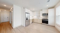 This thoughtfully designed one-bedroom, one-bathroom residence makes excellent use of its compact footprint, delivering a bright and modern living experience throughout. Light wood-tone flooring runs continuously across the entire unit, lending a cohesive and airy feel to every room.

The open-concept kitchen and living area serves as the heart of the home. The kitchen is outfitted with a two-tone cabinet scheme—crisp white upper cabinets with gold hardware paired with warm natural wood lower cabinets—complemented by a light tile backsplash and white countertops. A full suite of stainless steel appliances includes a side-by-side refrigerator with ice and water dispenser, a range, microwave, and dishwasher. The adjacent living area is bathed in natural light from large French doors fitted with blinds, and features a ceiling fan overhead.

The bedroom is a calm, neutral space with light walls and the same wood-tone flooring, offering a clean canvas for personalization. The bathroom features white tile flooring, a combination tub and shower with striking vertical gray tile, a built-in niche, and a light wood vanity.

Practical barn-style sliding doors line the hallway, leading to a dedicated in-unit laundry closet equipped with a Whirlpool front-load washer and overhead shelving.
