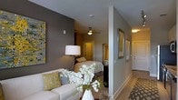 Located at 202 N West St in the heart of Raleigh, NC, this single-floor residence offers a thoughtfully designed living space with a cohesive and modern aesthetic. The interior is characterized by warm gray walls, crisp white trim, and durable wood-style flooring that flows throughout the space, creating a unified and inviting atmosphere.

The living area is bright and welcoming, furnished with a plush white sofa accented by mustard yellow and gray throw pillows. A bold abstract artwork on the wall adds a contemporary artistic touch, complementing the neutral color palette with pops of yellow and black. A floral arrangement serves as a stylish focal point, enhancing the overall décor.

Seamlessly connected to the living area, the bedroom features a ceiling fan with integrated lighting, providing both comfort and functionality. The room is finished with the same warm tones and benefits from soft, ambient lighting. Framed artwork adorns the hallway walls, adding character to the transitional spaces.

The entry corridor is well-lit and neatly finished, with a patterned area rug grounding the entryway. The layout is efficient yet comfortable, making excellent use of the single-floor footprint. Overall, this Raleigh residence combines contemporary design elements with practical living features for a polished and comfortable environment.