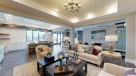 This well-appointed single-floor community space combines contemporary design with a welcoming, functional layout. The main lounge area serves as the heart of the space, featuring a tray ceiling adorned with a striking multi-arm chandelier, recessed lighting, and soft neutral tones. Plush seating arrangements centered around dark wood coffee tables create an inviting environment for gathering and relaxation, complemented by curated artwork and coastal-inspired accents.

Adjacent to the lounge, a spacious game and entertainment area opens seamlessly, providing ample room for socializing and recreation, including a billiards table. Large windows along this zone allow abundant natural light and views to the exterior. A well-equipped kitchenette nearby features crisp white cabinetry, quartz countertops, a wall-mounted television, rustic floating wood shelves, pendant lighting, and a central island with bar seating — ideal for events and casual gatherings.

The corridors are finished with warm hardwood flooring and shiplap-accented tray ceilings, guiding visitors through the space with an elegant, polished feel. A glass-enclosed private office with a dedicated seating area outside offers a professional setting for meetings or focused work. Throughout, the thoughtful blend of textures, neutral palettes, and contemporary furnishings creates a cohesive, upscale atmosphere suited for both community engagement and quiet retreat.