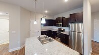 Located at 1555 Harris Rd in Fort Mill, South Carolina, this single-floor home offers a well-designed layout with a clean, neutral aesthetic throughout. The kitchen is a standout feature, equipped with rich dark cabinetry, granite-style countertops, a white subway tile backsplash, stainless steel appliances including a refrigerator, range, and microwave, and a peninsula island with a double sink illuminated by pendant lighting. Warm hardwood-style flooring grounds the kitchen and adjacent areas. The bedrooms are carpeted and bathed in natural light through multiple windows fitted with blinds, each room featuring a ceiling fan for added comfort. The primary bedroom includes access to a spacious walk-in closet outfitted with wire shelving systems for generous storage. The primary bathroom offers a dark-cabineted vanity, a large mirror with Hollywood-style lighting, and a glass-enclosed shower. A secondary full bathroom provides a shower-tub combination and a matching dark vanity. A dedicated laundry area houses a full-size washer and dryer set with overhead wire shelving. The home's consistent use of neutral tones, white trim, and thoughtful finishes creates a cohesive and functional living environment.