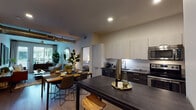 This contemporary single-floor residence is thoughtfully designed with a cohesive modern aesthetic that runs throughout every room. The open-concept layout connects the kitchen, dining, and living areas seamlessly, creating an inviting flow ideal for both everyday living and entertaining. The kitchen is outfitted with sleek two-tone cabinetry in light wood and dark finishes, stainless steel appliances including a range, microwave, dishwasher, and refrigerator, complemented by a white subway tile backsplash and dark countertops. A kitchen island with bar seating extends naturally into the dining area. The living room is bright and welcoming, featuring large windows and French doors that open to an outdoor area, allowing abundant natural light and views of the surrounding greenery. The bedroom offers a calm retreat with hardwood-style flooring, a large window with outdoor views, and clean, neutral walls. A versatile flex room serves as a comfortable secondary lounge or home office, complete with a window workspace. Two bathrooms mirror the home's modern palette, each featuring dark vanities, undermount sinks, large mirrors, and pendant lighting. Throughout the residence, wood-look flooring, recessed lighting, and curated wall art reinforce a polished, contemporary atmosphere.