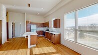 Located at 150 Leonard's Way in Elkhart Lake, Wisconsin, this single-floor, 2-bedroom, 1-bathroom residence offers a well-organized and efficiently designed layout. The kitchen is a standout feature, showcasing warm-toned wood cabinetry, light countertops, stainless steel appliances including a refrigerator, range, and dishwasher, and a central island that provides additional workspace and casual seating. Large windows flood the kitchen and living areas with abundant natural light, offering pleasant outdoor views of the surrounding landscape. Hardwood-style flooring runs throughout the main living areas, lending warmth and continuity to the space. A light-filled hallway connects the main living area to the two bedrooms, both of which are finished with neutral carpet and fitted with sliding wood-toned closet doors. The primary bedroom is generously proportioned and features a large window with outdoor views, filling the room with natural light. The bathroom includes in-unit stacked washer and dryer units, offering the convenience of on-site laundry alongside hardwood-style vinyl flooring. Throughout the residence, high ceilings and a neutral color palette create an open, airy ambiance suited to a variety of living arrangements.