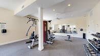 Located at 1420 Southern Ridge Ln in Charlottesville, VA, this dedicated fitness center offers a generously sized, single-floor workout space designed to accommodate a wide range of exercise needs. The room features warm, neutral-toned walls and durable carpet flooring throughout, creating a clean and welcoming environment for exercise.

The space is outfitted with an impressive selection of equipment, including multiple treadmills, an elliptical, a multi-station cable machine, a seated leg press, adjustable weight benches, and a full rack of dumbbells — providing options for both cardiovascular training and strength work. Protective floor mats are positioned beneath key equipment areas.

Large wall-mounted mirrors span a significant portion of the room, enhancing the sense of openness and allowing users to monitor their form during workouts. Recessed ceiling lighting, paired with ceiling fans, ensures the space remains well-lit and comfortable during use. Natural light filters in through multiple windows, adding brightness and a connection to the outdoors.

Structural columns are integrated into the layout, and the room benefits from clearly defined zones for cardio, strength training, and free weights. Multiple entry doors provide convenient access. The overall design is practical, functional, and thoughtfully appointed for an effective fitness experience.