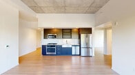 Located in Portland's vibrant SE Belmont neighborhood, this modern 3-bedroom, 2-bathroom residence offers a thoughtfully designed single-floor layout. The open living area makes a strong architectural statement with soaring exposed concrete ceilings and light hardwood flooring throughout, creating an industrial-chic aesthetic balanced by clean white walls and abundant natural light. Large black-framed windows frame neighborhood views, filling the living space with sunlight and a connection to the surrounding urban environment.

The kitchen is a standout feature, equipped with two-tone cabinetry — dark upper cabinets paired with navy lower units — complemented by white quartz countertops, a farmhouse-style sink, a white tile backsplash, and a full suite of stainless steel appliances including a gas range, built-in microwave, dishwasher, and french door refrigerator.

The primary bedroom offers a comfortable footprint with large windows overlooking the street, while the additional bedrooms provide flexible use with the same consistent hardwood flooring and concrete ceiling details. Both bathrooms are finished with dark wood vanities, white countertops, backlit mirrors, and tub-shower combinations. A hallway houses a space-saving stacked washer and dryer unit alongside closet storage, adding everyday convenience to this well-appointed urban residence.