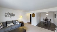 This single-floor, two-bedroom, one-bathroom residence offers a well-organized layout designed for comfortable everyday living. The living room serves as the heart of the home, featuring neutral-toned carpet that adds warmth underfoot and smooth white ceilings that keep the space feeling open and airy. A large wall provides ample room for personalized décor, while a central entryway connects the living area seamlessly to the rest of the home. Dark hardwood-style flooring transitions into the hallway and dining area, creating a clear visual distinction between spaces and adding a refined contrast to the lighter tones of the living room. The hallway leads to the two bedrooms, offering a sense of privacy and separation from the main living spaces. The dining area is situated just off the main corridor, making it convenient for everyday meals or entertaining. The overall layout promotes easy circulation between rooms, with open sightlines that enhance the sense of space. Crisp white walls throughout provide a clean, neutral backdrop that works well with a variety of décor styles. This residence combines functional design with a straightforward, practical floor plan suited for a range of lifestyles.