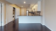 Located at 34 Prospect St in Hartford, Connecticut, this single-floor unit offers a well-designed layout with modern finishes throughout. The kitchen is a standout feature, showcasing white cabinetry extending to the ceiling, dark granite countertops, a mosaic tile backsplash, and a full suite of stainless steel appliances including a refrigerator, range, microwave, and dishwasher. Rich, dark hardwood flooring runs throughout the kitchen and living areas, lending a polished, contemporary feel. A peninsula with granite countertop provides additional workspace and separates the kitchen from the open living area, which is illuminated by recessed lighting. A dedicated laundry area with a washer is conveniently tucked away near the entry. The bedroom features neutral-toned carpeting, a window allowing natural light, and direct access to the hallway leading to the bathroom. The bathroom is finished with large-format tile flooring, a dark-cabinetry vanity with a rich countertop, a framed mirror, and a window for ventilation. Neutral warm tones and clean lines are consistent throughout, creating a cohesive and functional living environment.