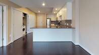 Located at 34 Prospect St in Hartford, Connecticut, this single-floor unit offers a well-designed layout with modern finishes throughout. The kitchen is a standout feature, showcasing white cabinetry extending to the ceiling, dark granite countertops, a mosaic tile backsplash, and a full suite of stainless steel appliances including a refrigerator, range, microwave, and dishwasher. Rich, dark hardwood flooring runs throughout the kitchen and living areas, lending a polished, contemporary feel. A peninsula with granite countertop provides additional workspace and separates the kitchen from the open living area, which is illuminated by recessed lighting. A dedicated laundry area with a washer is conveniently tucked away near the entry. The bedroom features neutral-toned carpeting, a window allowing natural light, and direct access to the hallway leading to the bathroom. The bathroom is finished with large-format tile flooring, a dark-cabinetry vanity with a rich countertop, a framed mirror, and a window for ventilation. Neutral warm tones and clean lines are consistent throughout, creating a cohesive and functional living environment.