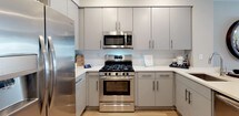 This well-designed single-floor residence offers a thoughtfully arranged layout that balances comfort and contemporary style. The kitchen is outfitted with light gray flat-front cabinetry, white quartz countertops, stainless steel appliances including a gas range, over-the-range microwave, and a French door refrigerator. A kitchen island with bar seating provides additional prep space and a casual dining option, flowing seamlessly into the open-concept dining and living areas. Light hardwood-style flooring runs throughout the main living spaces, creating a warm and cohesive look.

The living room is generously proportioned, featuring a large window that brings in natural light and a curated gallery wall arrangement. The dining area connects naturally to both the kitchen and living space, making the layout ideal for entertaining.

The two bedrooms are comfortably sized, each featuring hardwood-style flooring, neutral wall tones, and windows that allow for natural light. The primary bedroom includes ample room for a full furniture suite, while the second bedroom offers a similarly restful atmosphere.

The bathroom is finished with large-format light tile flooring, a gray vanity with a bright mirror and vanity lighting, and a shower with a classic curtain enclosure. The overall design palette throughout the residence is modern and neutral, with consistent finishes that give the space a polished, unified character.