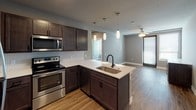 This well-appointed single-floor unit offers a thoughtfully designed layout with modern finishes throughout. The kitchen serves as a central highlight, featuring dark espresso cabinetry, white quartz countertops, a subway tile backsplash, and a full suite of stainless steel appliances including a refrigerator, electric range, microwave, and dishwasher. A peninsula with an undermount sink and matte black faucet provides additional prep space and opens seamlessly to the living area, which is finished with warm wood-look flooring and a ceiling fan to promote natural air circulation. Natural light filters in through sizable windows fitted with blinds. The bedroom is carpeted for comfort and includes a ceiling fan, generous closet space, and a spacious walk-in closet outfitted with wire shelving systems for organized storage. Two bathrooms serve the unit: one features a dark-toned vanity with white countertop, a matte black faucet, a large mirror, and a soaking tub with shower, while the second bathroom offers a walk-in shower with sliding glass doors, a matching dark vanity, and a built-in linen closet with louvered doors. Wood-look flooring extends throughout the wet areas, tying the design together with a cohesive, contemporary aesthetic.