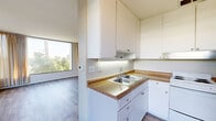 Located at 3737 Atlantic Ave in Long Beach, California, this single-floor unit is defined by its striking floor-to-ceiling windows that frame lush, tree-lined views from multiple rooms, flooding the interior with natural light throughout the day. The hardwood-style flooring runs consistently across the living areas, bedrooms, and hallways, lending a cohesive and clean aesthetic to the space.

The kitchen is laid out in an efficient U-shaped configuration, outfitted with white cabinetry extending to the ceiling for generous storage, warm-toned countertops, a double stainless steel sink, an electric range, and a full-size refrigerator. A dedicated dining or breakfast area adjacent to the kitchen benefits from a large picture window overlooking greenery.

The living area is particularly notable for its expansive corner windows on two walls, creating a panoramic view of the surrounding landscape and filling the room with sunlight. Each bedroom features its own oversized window, ceiling fan, and ample floor space, with views ranging from palm trees to neighborhood rooftops.

A hallway connects the rooms in an organized layout. The bathroom is well-appointed with a white vanity, tiled tub-shower combination with chrome fixtures and grab bars, and wood-look flooring, completing the unit with a clean, neutral finish throughout.