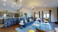 Located at 3660 Sterling Park Cir in Grove City, Ohio, this single-floor community space is thoughtfully designed to blend modern aesthetics with a warm, inviting atmosphere. The centerpiece of the interior is a dramatic vaulted ceiling that amplifies the sense of openness and airiness throughout the main living area. Two striking sputnik-style chandeliers serve as bold focal points, casting a warm, contemporary glow across the space. Rich hardwood-style flooring anchors the room, complementing the neutral wall tones and providing a sophisticated contrast to the vibrant blue area rug that defines the central lounge area. The open-concept layout seamlessly connects the lounge seating area — furnished with a charcoual sofa, accent chairs, and layered coffee tables — to a bar-height counter and kitchenette along one side, complete with cabinetry and bar stool seating. Large windows dressed with floor-length curtains line the walls, inviting abundant natural light and offering views of the surrounding greenery. A dedicated seating nook near the windows provides an additional area for relaxed conversation or individual use. Colorful abstract artwork adorns the walls, adding personality and energy to the overall design. This space strikes a confident balance between functional community use and polished interior design.
