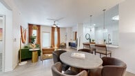 Located at 10221 Millstone Dr in Lenexa, KS, this single-floor residence offers a thoughtfully designed open-concept layout that seamlessly connects the living, dining, and kitchen areas. The living room features light wood-style flooring, a ceiling fan, and large windows with warm-toned curtains that fill the space with natural light. A round dining table sits adjacent to the kitchen, which is outfitted with stainless steel appliances, two-tone cabinetry — white upper cabinets paired with slate-gray lower cabinets — quartz countertops, a tile backsplash, and a center island providing additional prep and storage space. A hallway off the kitchen leads to the in-unit laundry area, complete with a full-size washer and shelving above. The primary bedroom offers plush carpeting, a ceiling fan, and a bold accent wall, while the second bedroom features a stylish two-tone painted wall and ample natural light. Both bedrooms provide a comfortable and private retreat. The bathroom includes a quartz vanity countertop, white cabinetry with brushed hardware, a large mirror, and a soaking tub with tile surround. Light wood-style flooring flows consistently throughout the main living areas, contributing to a cohesive and modern aesthetic throughout the home.
