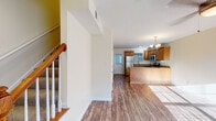 This two-story home in La Grange, Kentucky, offers a well-organized layout across two levels. The main floor features an open-concept living and kitchen area connected by durable hardwood-style flooring that runs throughout. The kitchen is equipped with stainless steel appliances, including a refrigerator, range, and built-in microwave, complemented by warm honey-toned cabinetry, granite-look countertops, and a peninsula that provides additional prep and seating space. A ceiling fan anchors the spacious living area, which receives generous natural light. A half bathroom with a wood-vanity and hardwood-style flooring is conveniently located on the main level. A carpeted staircase with a wooden handrail leads to the upper floor, where the bedrooms feature vaulted ceilings, ceiling fans, plush carpeting, and ample natural light from windows with blinds. The primary bedroom includes an en suite bathroom with a wide vanity, large mirror, and wood cabinetry. Additional bedrooms offer closets and vaulted ceilings. A dedicated utility space on the upper level houses the water heater and washer/dryer hookups with overhead wire shelving for storage.