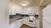 Located at 409 Tradewinds Dr in Fayetteville, NC, this single-floor residence offers a well-appointed layout designed for comfortable everyday living. The kitchen is a standout feature, showcasing white shaker-style cabinetry, granite-look countertops, a bold blue subway tile backsplash, and white appliances including a range, built-in microwave, and dishwasher. Wood-style flooring runs throughout the kitchen and main living areas, adding warmth and visual continuity. The living spaces are bright and open, with neutral beige walls and natural light streaming through multiple windows dressed with blinds. Bedrooms are finished with plush carpeting, ceiling fans for year-round comfort, and ample closet space — including a walk-in closet in the primary bedroom. The primary bedroom also provides direct access to a private en-suite bath featuring a soaking tub-shower combination with built-in shelving niches and a grab bar. A second full bathroom includes a tub-shower unit, toilet, and vanity with wood-style flooring. Textured ceilings are present throughout the home, contributing to its classic character. The overall ambiance is clean, functional, and move-in ready.