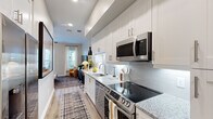 Located at 201 Pilot St in Savannah, GA, this thoughtfully designed one-bedroom, one-bathroom residence makes excellent use of its compact footprint. The galley-style kitchen is a standout feature, showcasing white shaker cabinetry extending to the ceiling, granite countertops, a subway tile backsplash, and a full suite of stainless steel appliances including an electric range, built-in microwave, and dishwasher. Pendant lighting adds a modern touch, while the open sightline into the living area enhances the sense of space. Light wood-tone flooring flows throughout the main living areas, complementing the neutral color palette. The generously sized bedroom serves as a private retreat, featuring a teal accent wall, ceiling fan, and floor-to-ceiling windows alongside a sliding glass door opening to a private balcony with outdoor views. The bedroom also connects to a walk-in closet outfitted with wire shelving systems for organized storage. The bathroom features white vanity cabinetry with granite countertops, a framed mirror, and light wood-tone flooring. A dedicated in-unit laundry area adds everyday convenience. Overall, the space offers a clean, contemporary aesthetic with practical layout and quality finishes throughout.