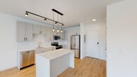 This single-floor unit at 1116 Missouri Ave in St. Louis, MO offers a clean, modern aesthetic defined by an open-concept design and a bright, neutral palette. Light hardwood flooring runs throughout the main living areas, complementing the crisp white walls and recessed lighting that collectively create an airy, well-lit atmosphere.

The kitchen is a standout feature, outfitted with shaker-style cabinetry in a soft gray-white finish, white quartz countertops, a subway tile backsplash, and a full suite of stainless steel appliances including a refrigerator, electric range, microwave, and dishwasher. A central island provides additional counter space and serves as a natural divider between the kitchen and the open living area. Stylish globe pendant lights and a black track lighting system add a contemporary industrial touch overhead.

The spacious living area benefits from natural light through multiple windows offering outdoor views, and flows seamlessly from the kitchen. A dedicated closet area adjacent to the bathroom provides organized storage with wire shelving and carpeted flooring. The bathroom includes a white shaker-style vanity with quartz countertop, black hardware accents, and a well-lit mirror. The overall ambiance is modern, clean, and move-in ready.