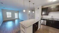 This single-story, 3-bedroom, 2-bathroom home in Austin, TX offers a well-designed open floor plan that seamlessly connects the kitchen and living areas. The kitchen is a standout feature, equipped with dark espresso cabinetry, granite countertops, a subway tile backsplash, stainless steel appliances — including a dishwasher, range, and refrigerator — and a central island with pendant lighting overhead. Crown molding adds a refined touch throughout the main living spaces, which feature durable hardwood-style flooring. The living room benefits from natural light via a window and exterior door access, lending an open, airy feel. The bedrooms are carpeted for comfort and include ceiling fans, windows with blinds, and closet access. The primary bedroom is a comfortable size and includes a walk-in closet with wire shelving systems on three walls. The two bathrooms are finished consistently with granite-topped dark vanities; one features a tub-shower combo with a subway tile surround and brushed nickel fixtures, while the other offers a clean, functional layout with tile flooring. The overall aesthetic is modern and cohesive, with neutral tones throughout.