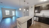 This single-story, 3-bedroom, 2-bathroom home in Austin, TX offers a well-designed open floor plan that seamlessly connects the kitchen and living areas. The kitchen is a standout feature, equipped with dark espresso cabinetry, granite countertops, a subway tile backsplash, stainless steel appliances — including a dishwasher, range, and refrigerator — and a central island with pendant lighting overhead. Crown molding adds a refined touch throughout the main living spaces, which feature durable hardwood-style flooring. The living room benefits from natural light via a window and exterior door access, lending an open, airy feel. The bedrooms are carpeted for comfort and include ceiling fans, windows with blinds, and closet access. The primary bedroom is a comfortable size and includes a walk-in closet with wire shelving systems on three walls. The two bathrooms are finished consistently with granite-topped dark vanities; one features a tub-shower combo with a subway tile surround and brushed nickel fixtures, while the other offers a clean, functional layout with tile flooring. The overall aesthetic is modern and cohesive, with neutral tones throughout.