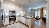 This 2-bedroom, 2-bathroom residence is thoughtfully designed across a single floor, offering a cohesive open-concept layout that connects the kitchen and living area seamlessly. The kitchen is a standout feature, equipped with stainless steel appliances including a range, microwave, and dishwasher, complemented by white shaker cabinetry, granite countertops, a subway tile backsplash, and a central island with pendant lighting overhead. Hardwood-style flooring runs throughout the unit, adding warmth and visual continuity.

The living room benefits from large windows that invite natural light and feature a ceiling fan for added comfort. Both bedrooms are well-sized, each with windows dressed in floor-length curtains and ceiling fans. The primary bedroom includes access to a walk-in closet outfitted with multi-level shelving and hanging rods.

The two bathrooms differ in configuration: the primary bath offers a glass-enclosed walk-in shower and a granite-topped double vanity, while the secondary bath features a soaking tub with tiled surround and a single vanity with matching granite countertop. Neutral tones and consistent finishes throughout create a cohesive, modern ambiance.