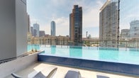 Perched high above the Dallas cityscape, this stunning rooftop amenity deck offers an exceptional outdoor experience defined by modern design and sweeping urban views. The centerpiece is a sleek infinity-edge pool with crisp blue tile, positioned to frame dramatic panoramic views of the Dallas skyline, including the iconic Reunion Tower and surrounding high-rise towers. A glass railing system borders the pool deck, ensuring unobstructed sightlines across the city in every direction.

Surrounding the pool, a generously sized sun deck is outfitted with contemporary lounge chairs and chaise seating, ideal for relaxing in the open air. A covered corridor runs along the perimeter, featuring a warm wood-paneled ceiling supported by clean architectural columns, providing shade and an elegant contrast to the open sky beyond.

The social areas include an outdoor bar with counter-height seating, a ping pong table, oversized lawn games, and comfortable lounge groupings — all thoughtfully arranged to encourage gathering. Lush plantings and dark decorative stone accents add texture and greenery throughout the space.

Whether enjoying a morning swim with skyline views or an evening at the bar under the open sky, this rooftop deck delivers a polished, resort-inspired atmosphere in the heart of Dallas.