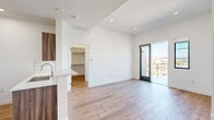 This contemporary single-floor residence showcases a clean, modern aesthetic defined by crisp white walls, soaring ceilings, and warm wood-tone flooring that flows seamlessly throughout the living spaces. The open-concept layout connects the living area to the kitchen, creating a bright and airy atmosphere enhanced by abundant natural light.

The kitchen is thoughtfully designed with rich wood-grain cabinetry, a striking white subway tile backsplash, quartz countertops, and a peninsula with an integrated sink — ideal for both cooking and casual dining. Stainless steel appliances, including a gas range, over-the-range microwave, and a French door refrigerator, complete the space.

The generously sized living area opens directly to a private balcony through sleek black-framed glass doors, offering expansive city views. Additional rooms provide versatile living space, each featuring the same wood flooring and large black-framed windows that flood the interiors with daylight while framing the surrounding urban skyline.

A walk-in closet offers excellent storage, while a secondary bedroom features a modern mirrored sliding closet door. The bathroom is finished with large-format neutral tiles, a wood-toned vanity with a white countertop, and an illuminated mirror, delivering a clean and refined look throughout.